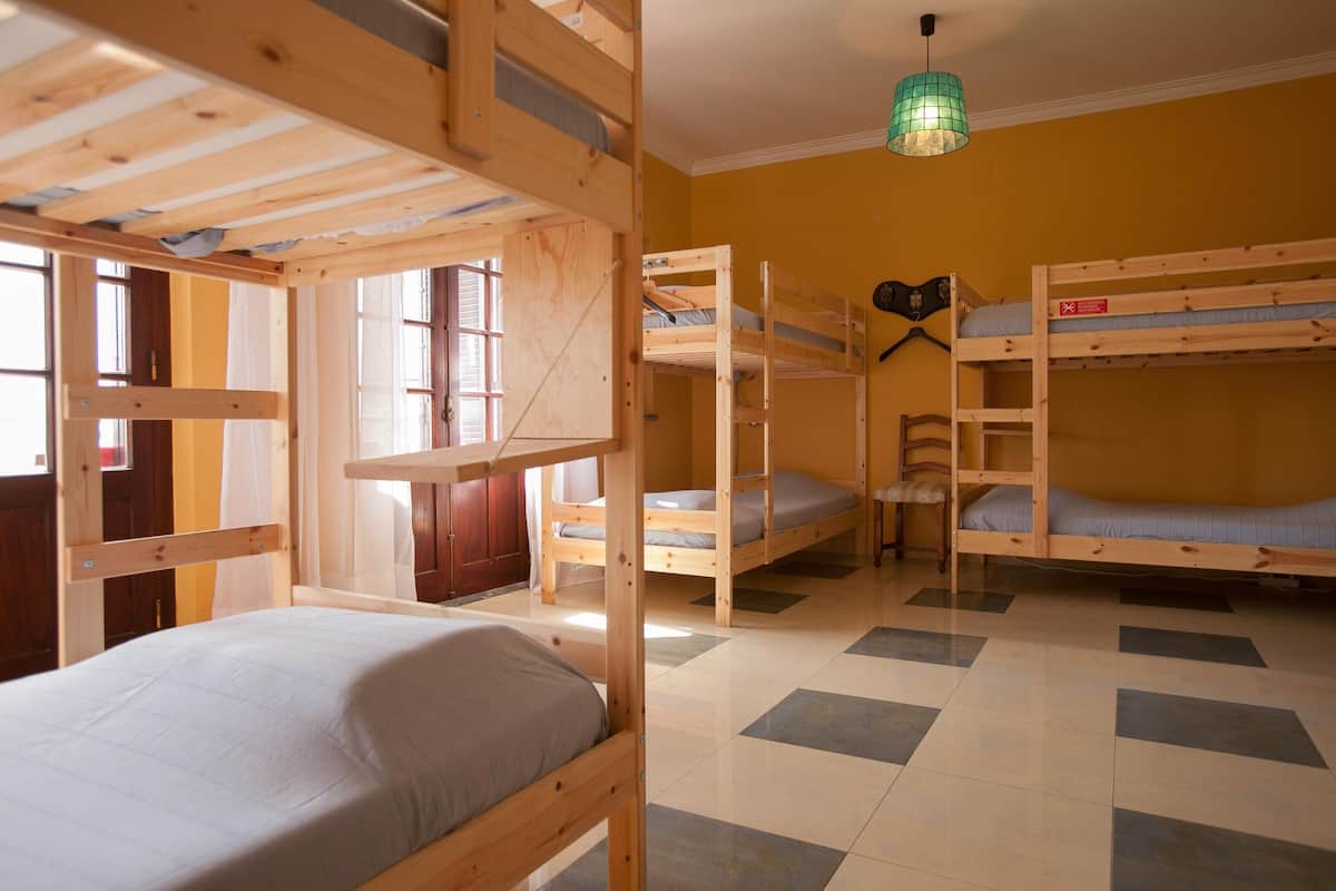 A room with bunk beds, a window with curtains, a green hanging light, and a tiled floor.