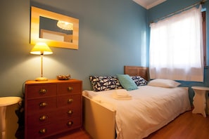 Quarto com cama, penteadeira, luminária e janela com cortinas.