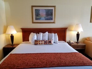 Quarto de hotel com uma cama grande, duas luminárias de cabeceira, um quadro na parede e um edredom vermelho estampado.