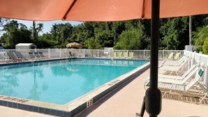 A swimming pool with lounge chairs and umbrellas, surrounded by a white fence. - Sun Inn & Suites (Kissimmee)