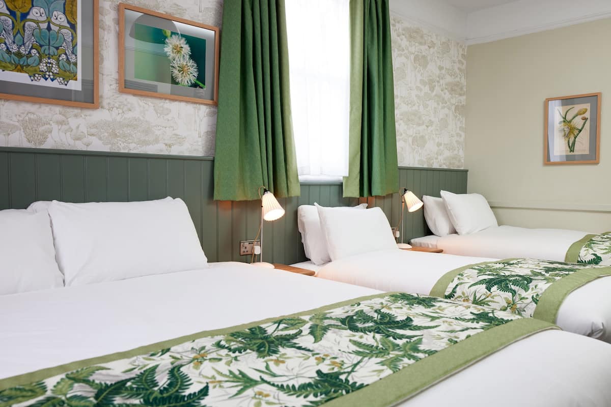 A hotel room with two beds, green curtains, floral bedspreads, and artwork on the walls.
