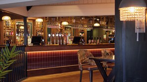 A bar area with a wooden counter, bar stools, and a variety of bottles and glasses.