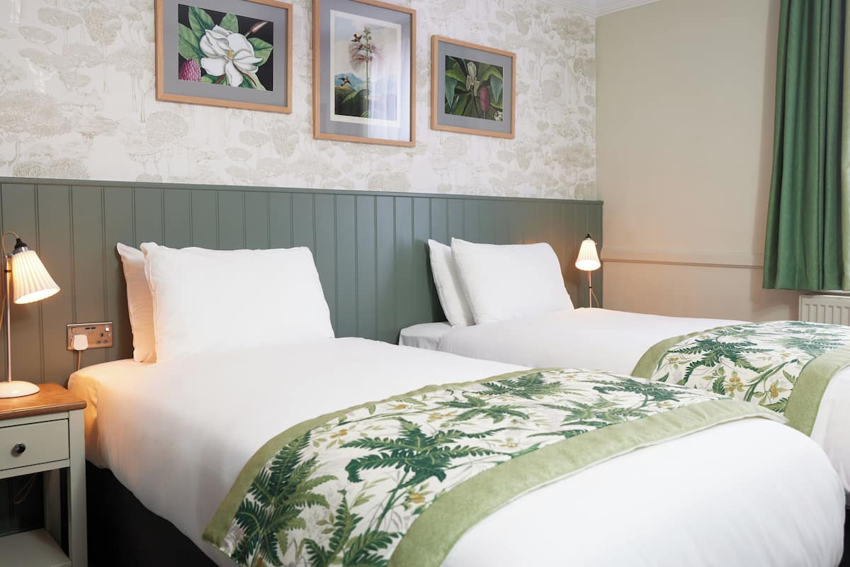 A hotel room with two beds, a green headboard, and floral wall art.