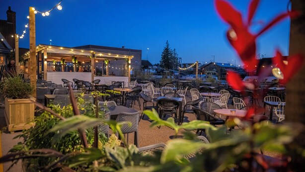 An outdoor patio area with tables and chairs, string lights, and a building in the background.