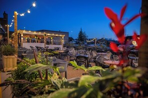 An outdoor patio area with tables and chairs, string lights, and a building in the background. - Kings Head Hotel by Greene King Inns (Norwich)