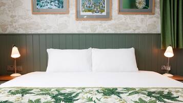 Una cama bien hecha con sábanas blancas, una colcha con estampado de hojas verdes y dos lámparas de noche.