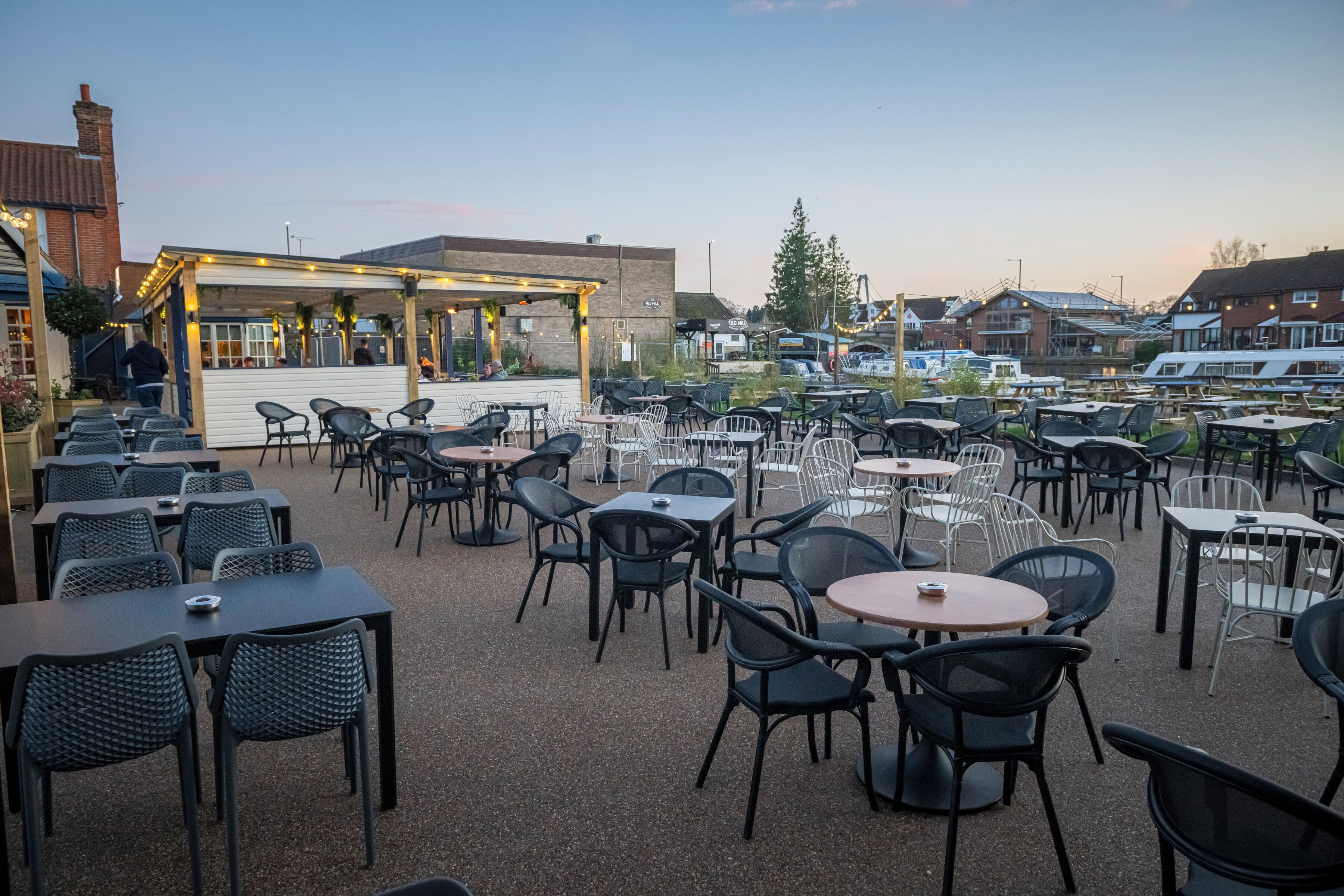 An outdoor patio with multiple tables and chairs, a covered seating area, and a view of residential buildings in the background.