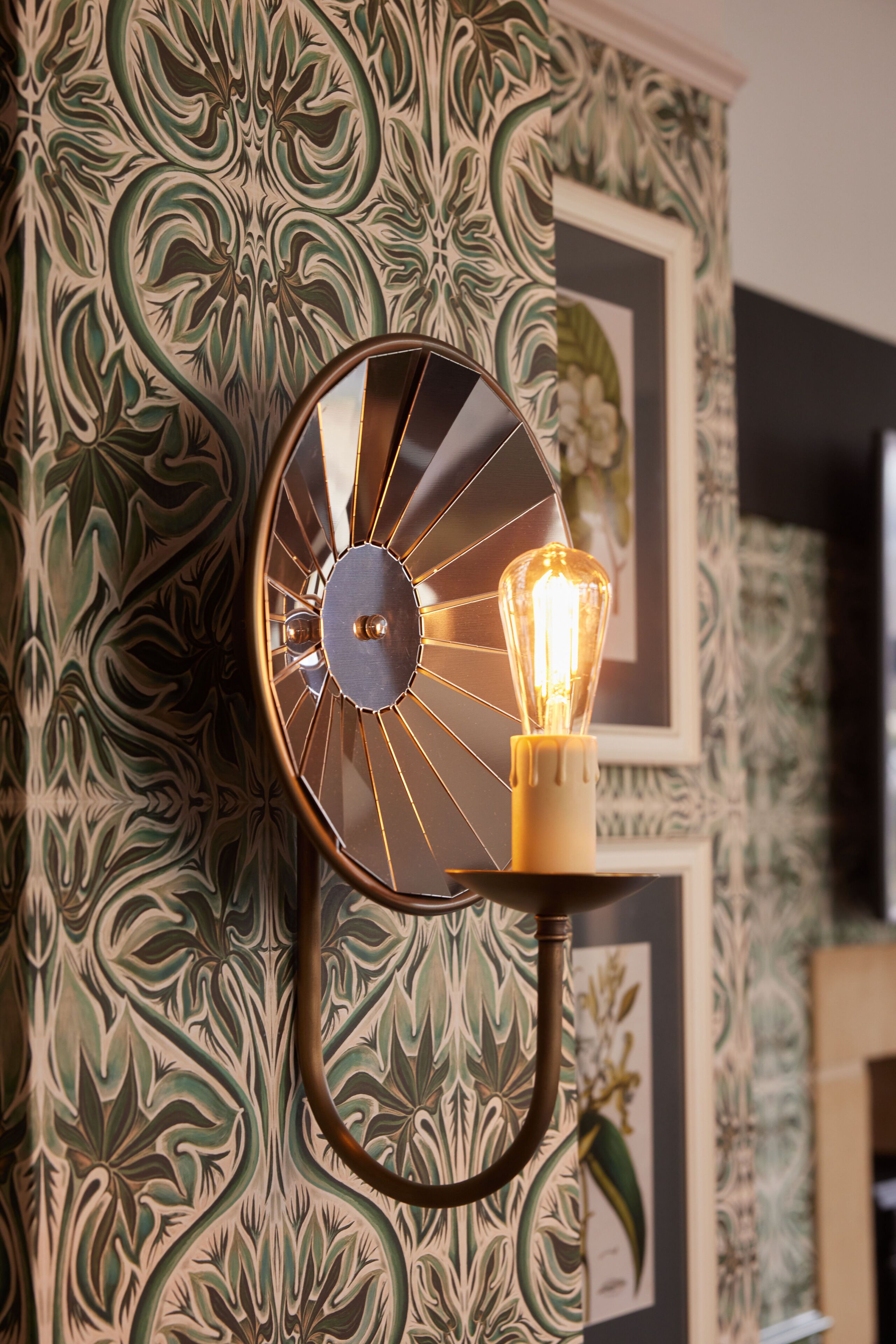Un luminaire mural fixé au mur, avec une ampoule visible, placé devant un papier peint à motifs.