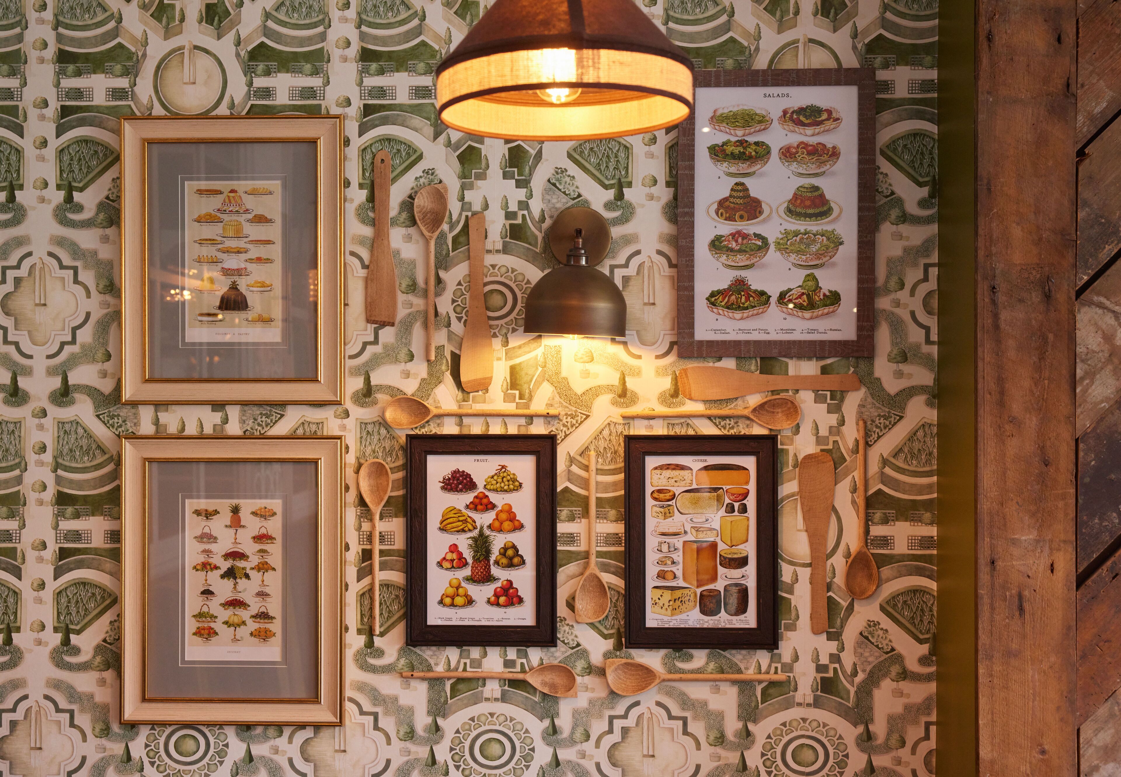 A wall with framed food illustrations and wooden spoons.