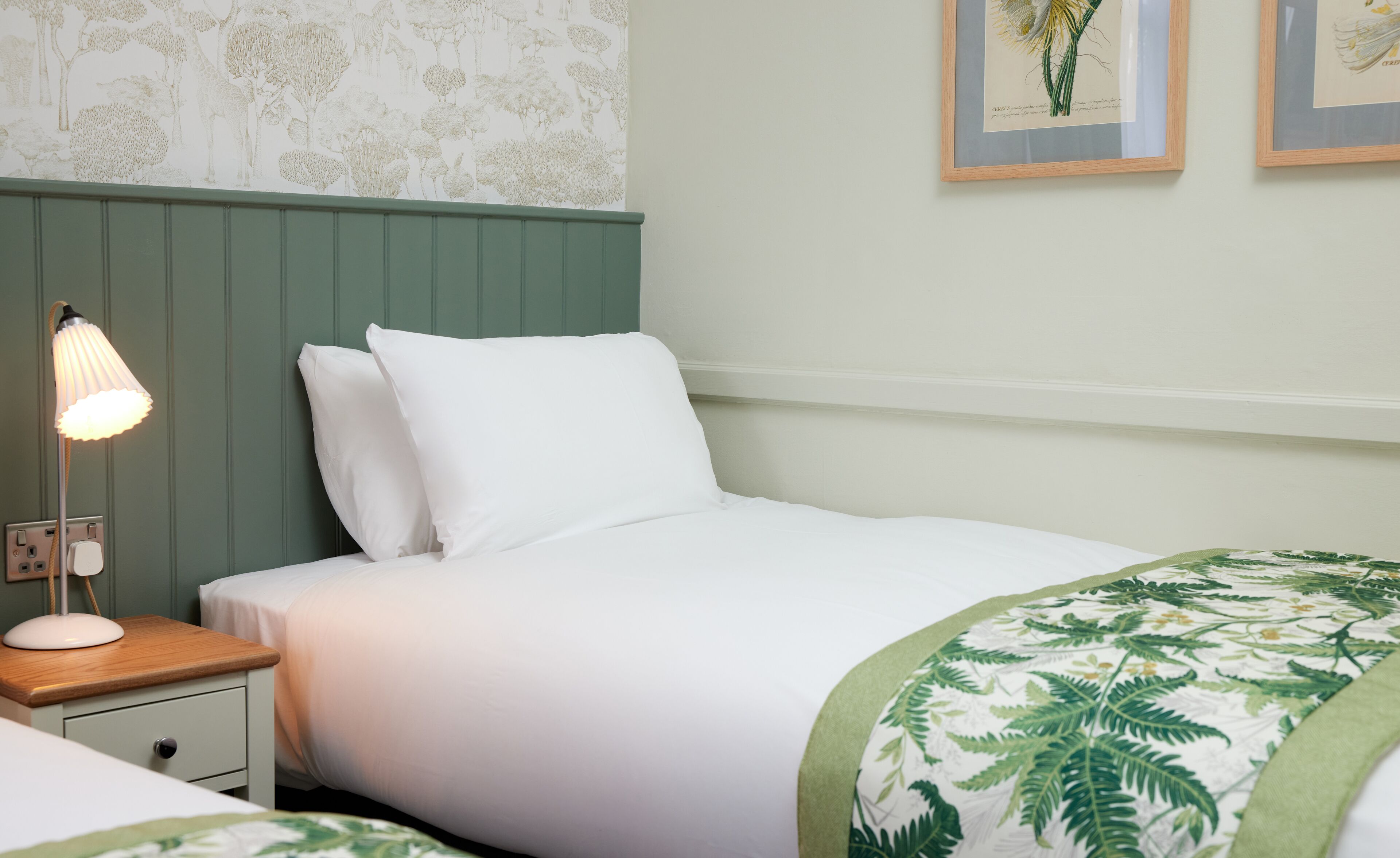 A neatly made bed with white linens, a green headboard, and a bedside lamp.