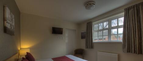 Una habitación de hotel con cama, sillón, televisor, ventana con cortinas y radiador.