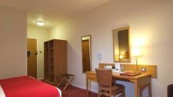 A hotel room with a bed, a desk, a chair, a mirror, and a television.