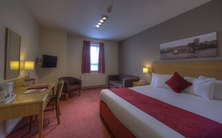 Habitación de hotel con cama, escritorio, silla, televisor y ventana con cortinas.