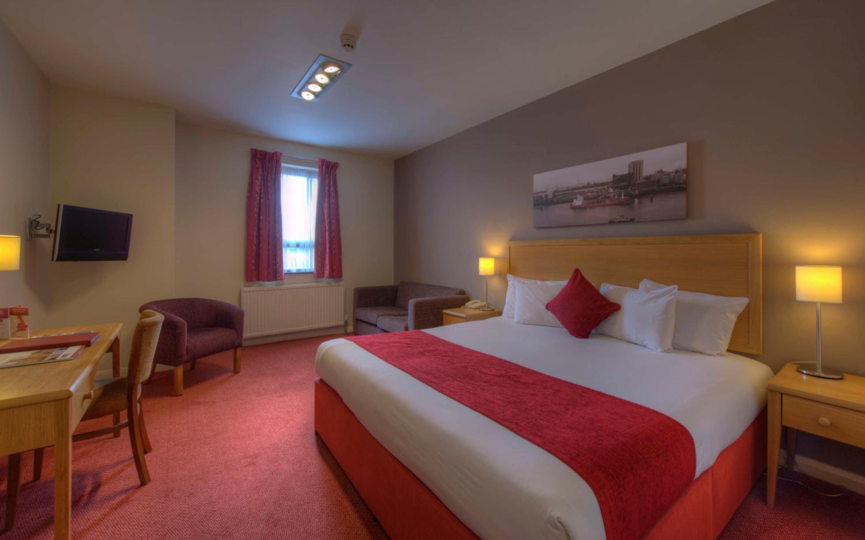 A hotel room with a large bed, a desk, a chair, a TV, and a window with curtains.