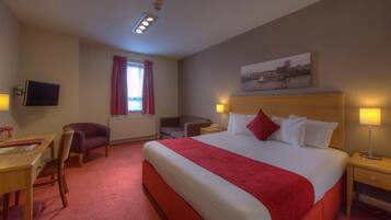 A hotel room with a large bed, a desk, a chair, a TV, and a window with curtains.