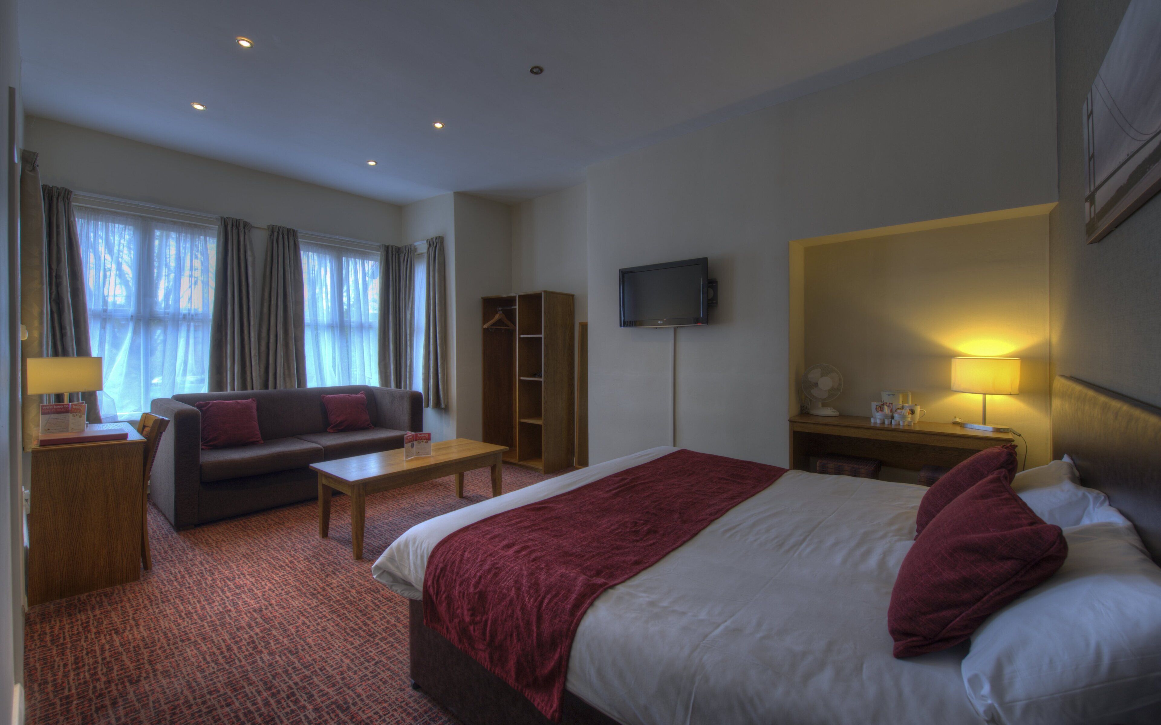 A hotel room with a bed, a sofa, a desk, a TV, and a wardrobe.