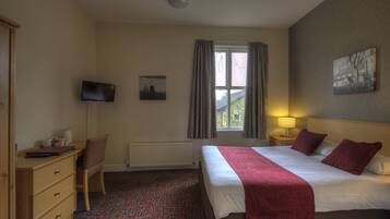 Una camera d'albergo con un letto, una scrivania, una sedia, una televisione, una finestra con tende e un quadro appeso al muro.