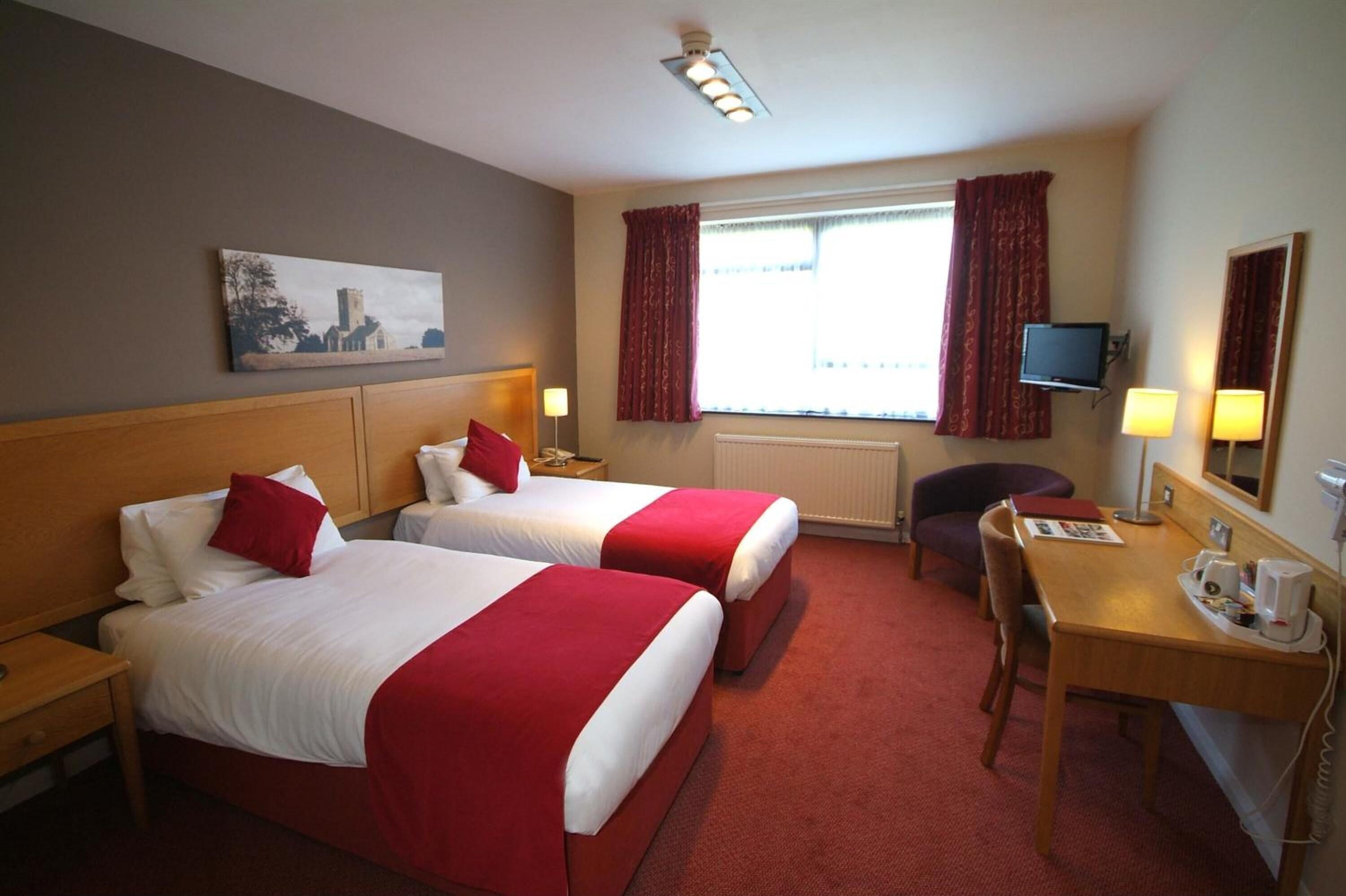 A hotel room with two beds, a desk, a chair, a TV, and a window with curtains.