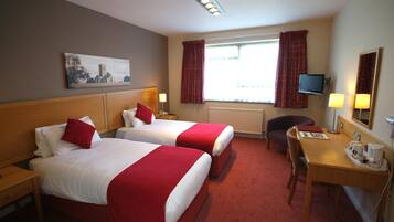 A hotel room with two beds, a desk, a chair, a TV, and a window with curtains.