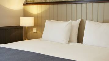 A hotel room with a bed, pillows, a nightstand, and a lamp.