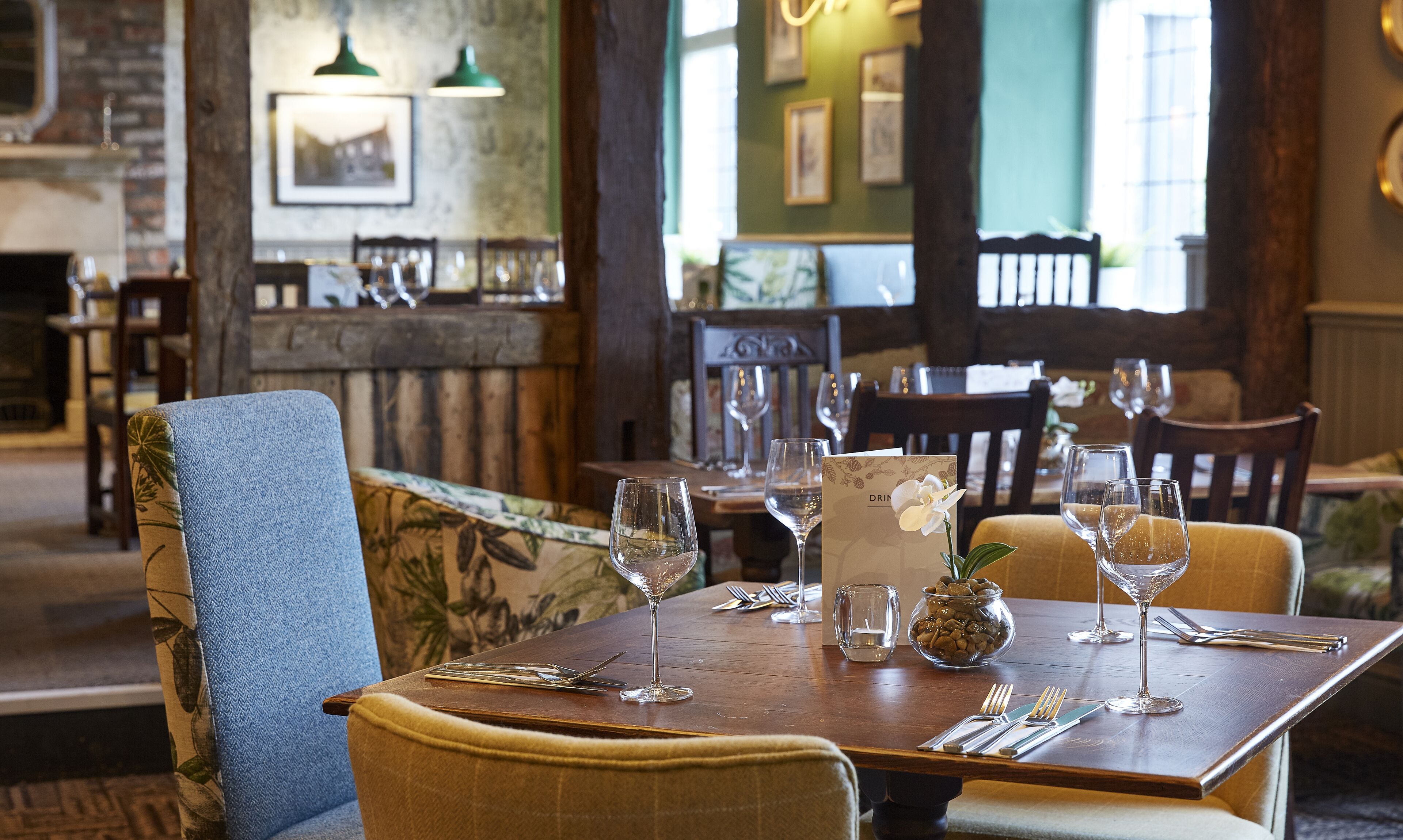 A dining area with a wooden table set for two, featuring wine glasses, cutlery, and a menu.