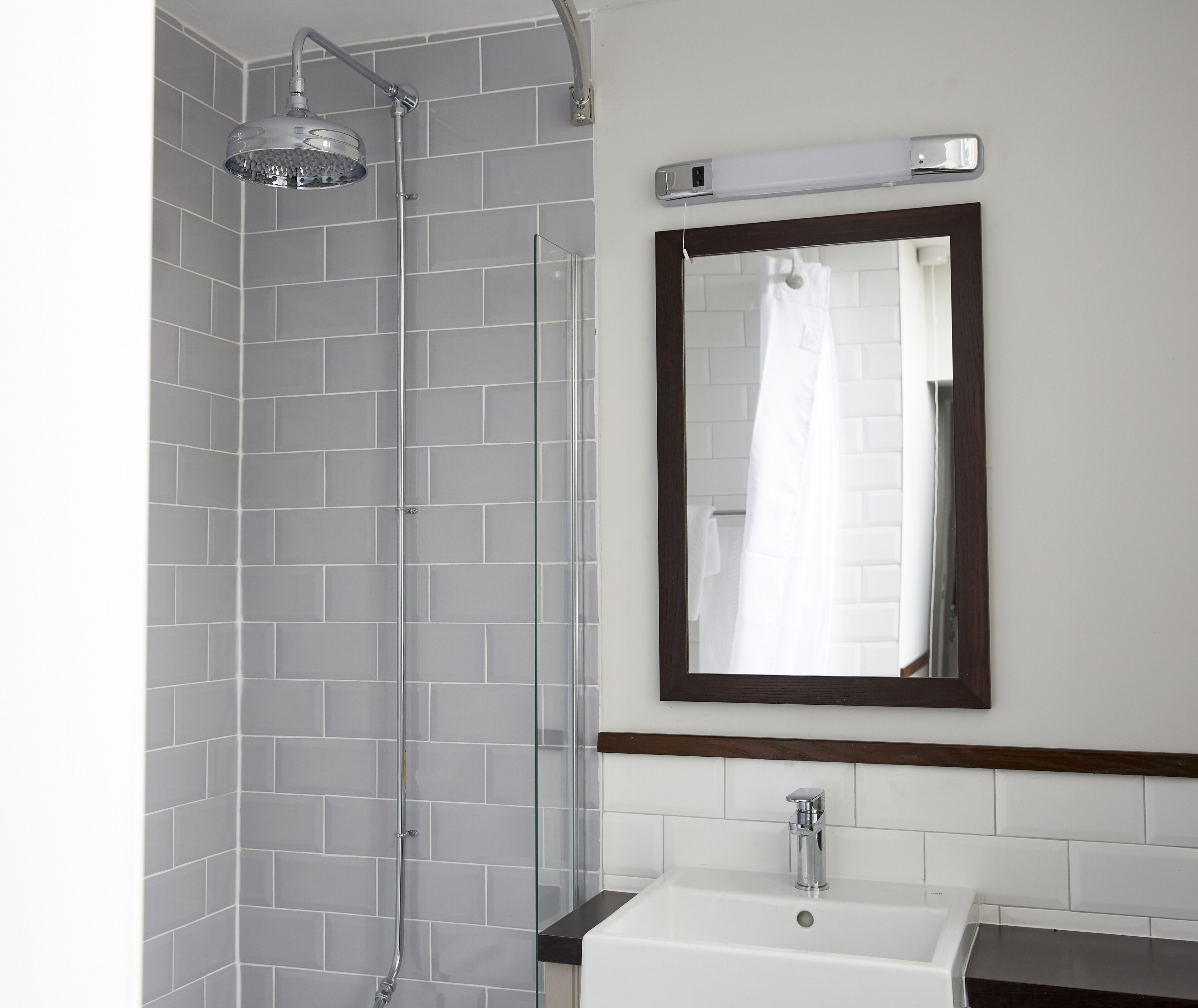 Une salle de bain avec une douche à parois de verre, un lavabo blanc et un miroir avec un cadre en bois.