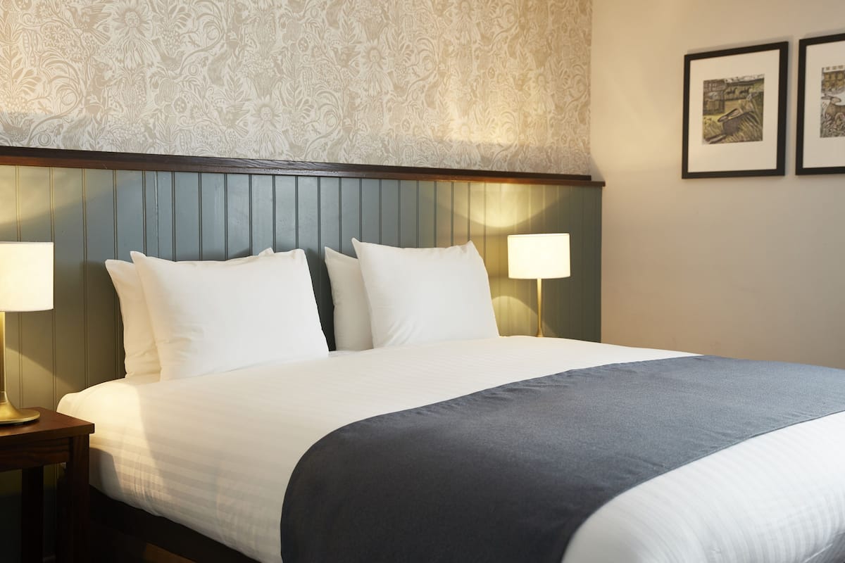 A neatly made bed with white and grey bedding, two bedside lamps, and a patterned wallpaper.