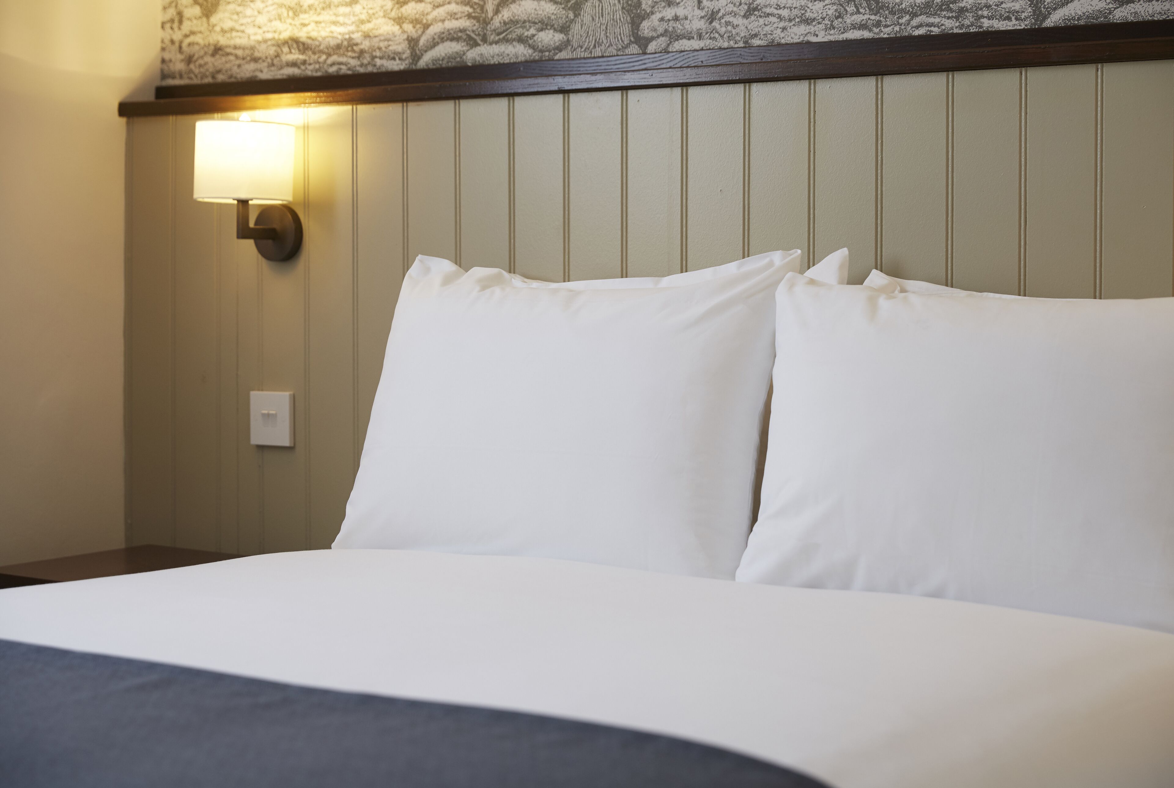 A hotel room with a bed, a wall-mounted light, and a textured wall design.