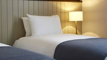 Una habitación de hotel con cama, almohadas, una lámpara de noche y cabecera con líneas verticales.