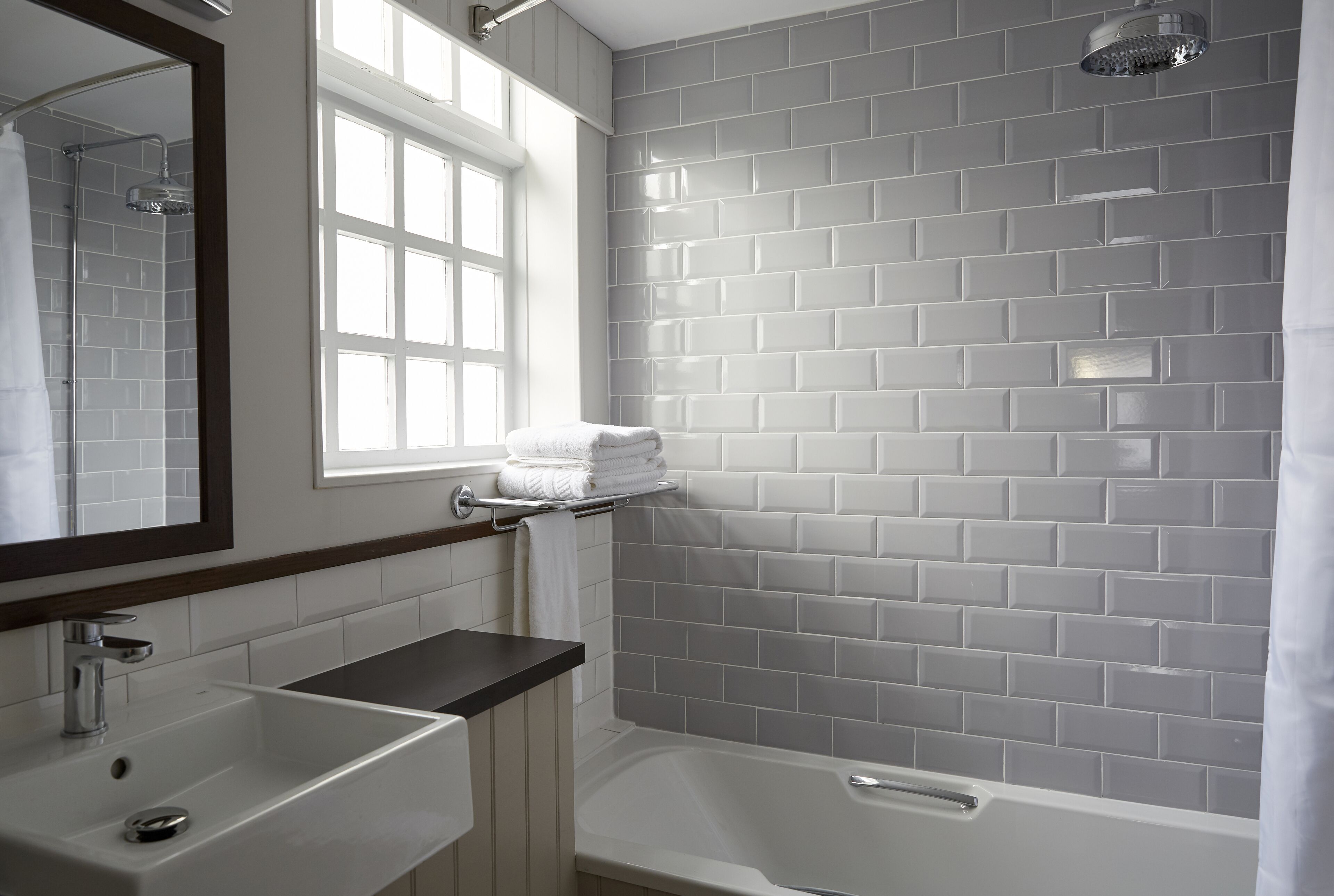 A bathroom with a white sink, a mirror, a window, and a shower area.