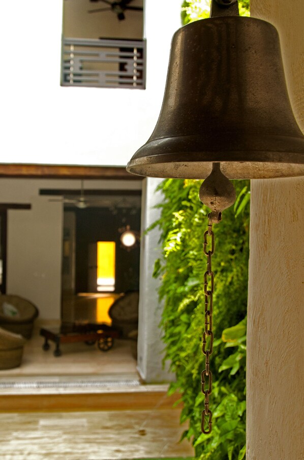 Una campana cuelga de un pilar en una habitación con vista a un comedor y follaje verde al exterior.