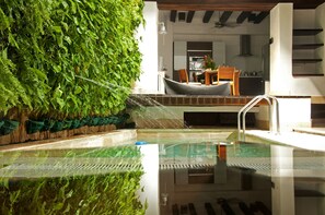 Piscina com fundo de vidro, cercada por vegetação exuberante e um deck de madeira.