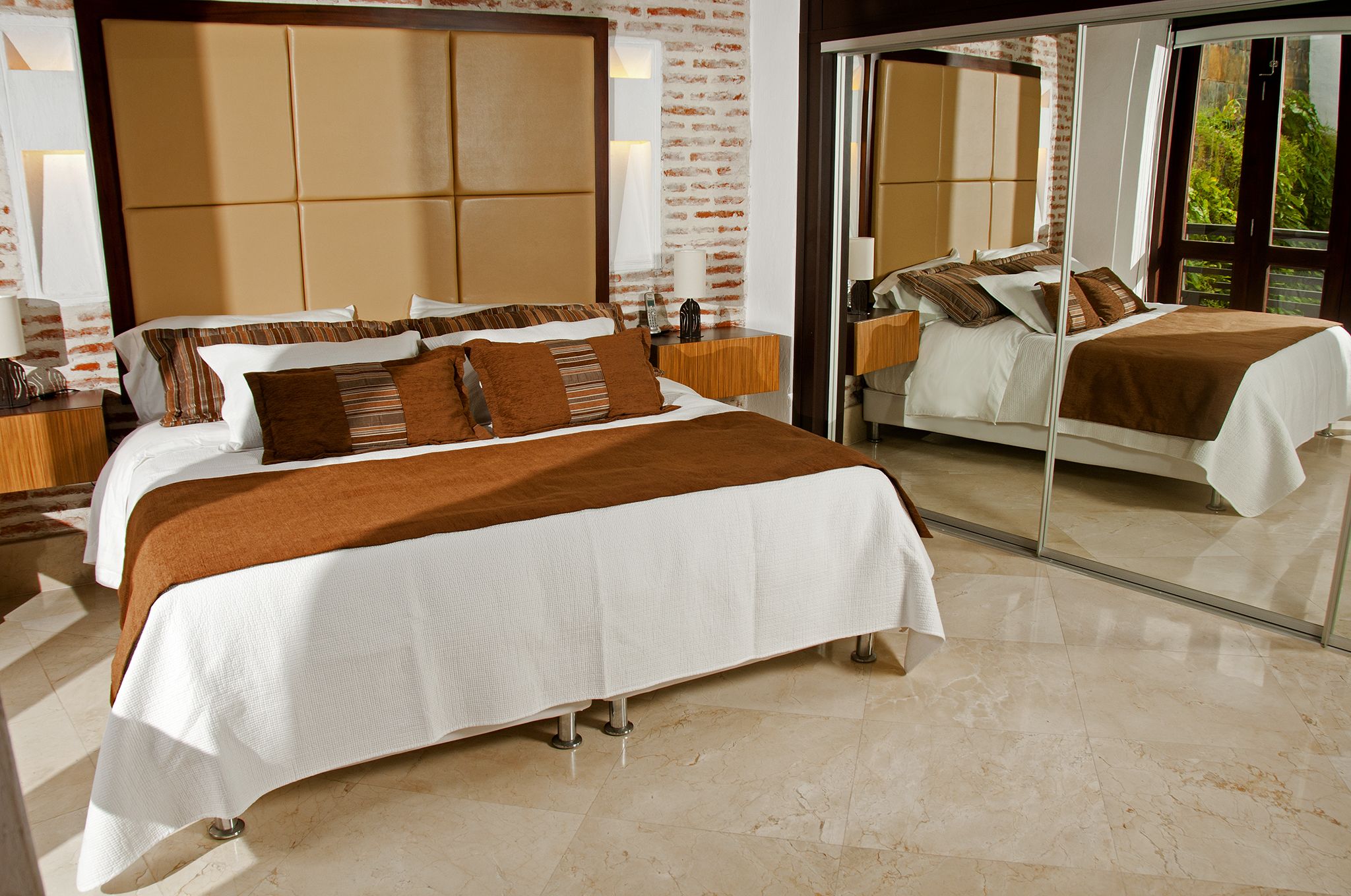 A modern hotel room with a large bed, a mirror, and a view of greenery outside.