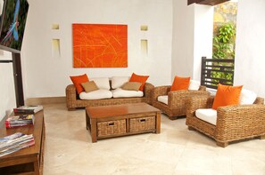 A living room with wicker furniture, a coffee table, and a large orange abstract painting on the wall.