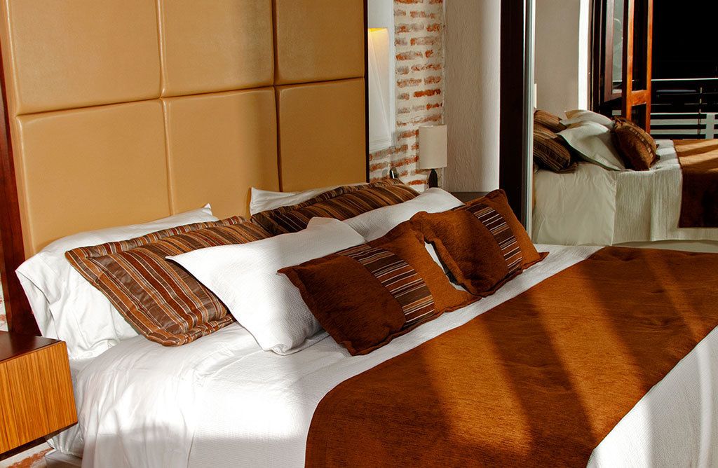 A neatly made bed with striped and solid brown pillows, a white bedspread, and a brown throw blanket.