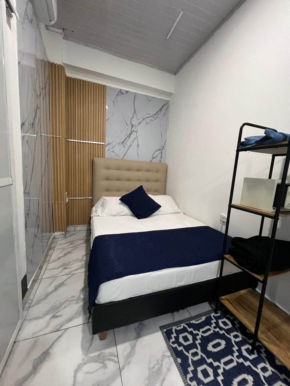 A bedroom with a bed, a wardrobe, a patterned rug, and a marble wall.