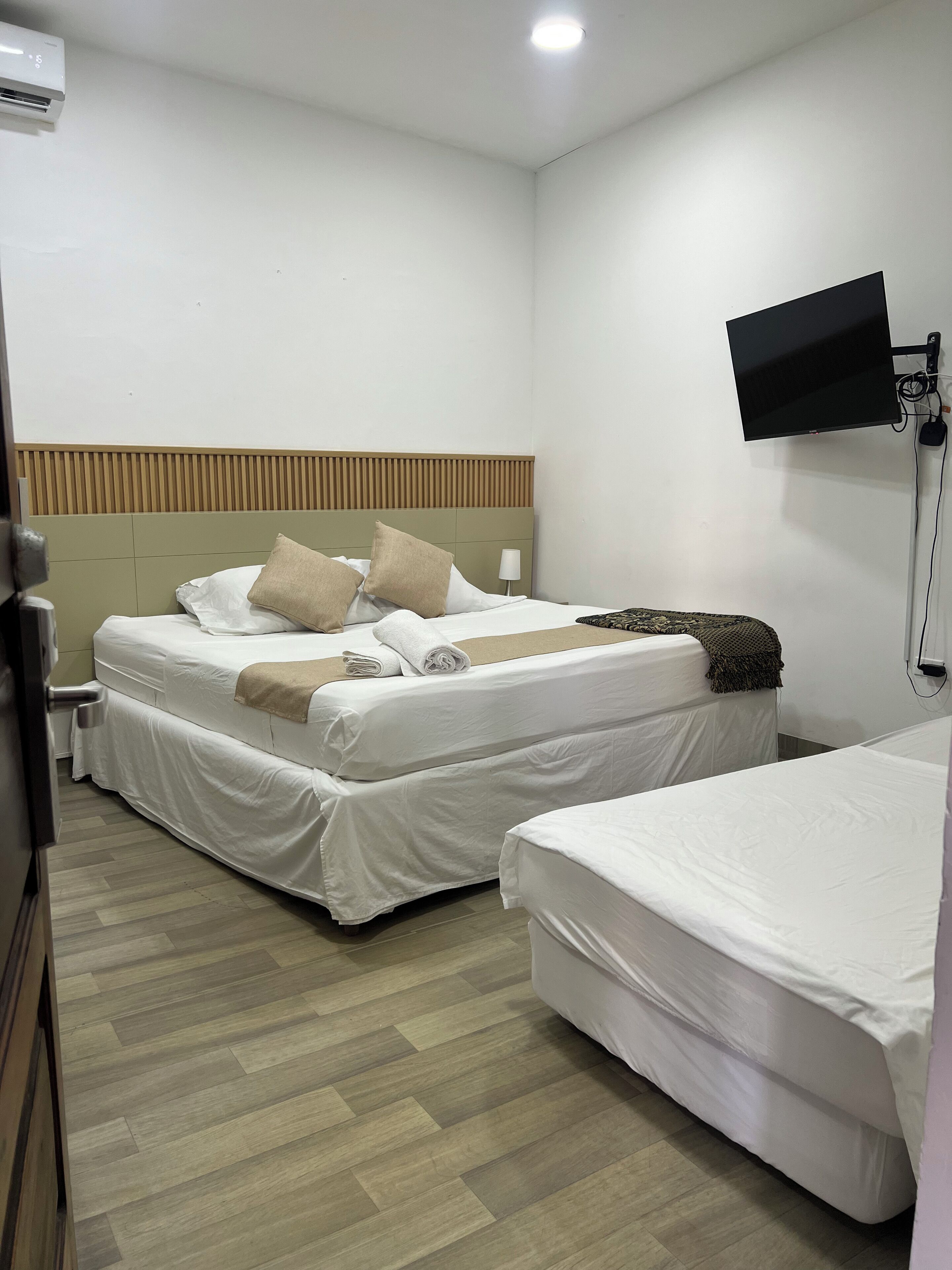 Ein Hotelzimmer mit zwei Betten, einem an der Wand montierten Fernseher und einem hölzernen Kopfteil.