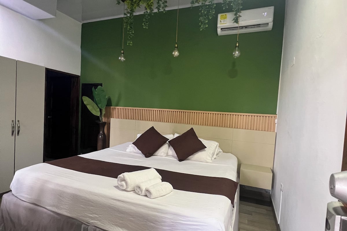 A hotel room with a large bed, a green accent wall, and a ceiling fan.