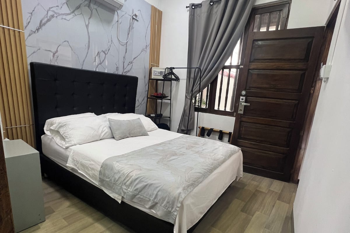 A bedroom with a bed, a wardrobe, a small table, a hanging light, and a window with curtains.