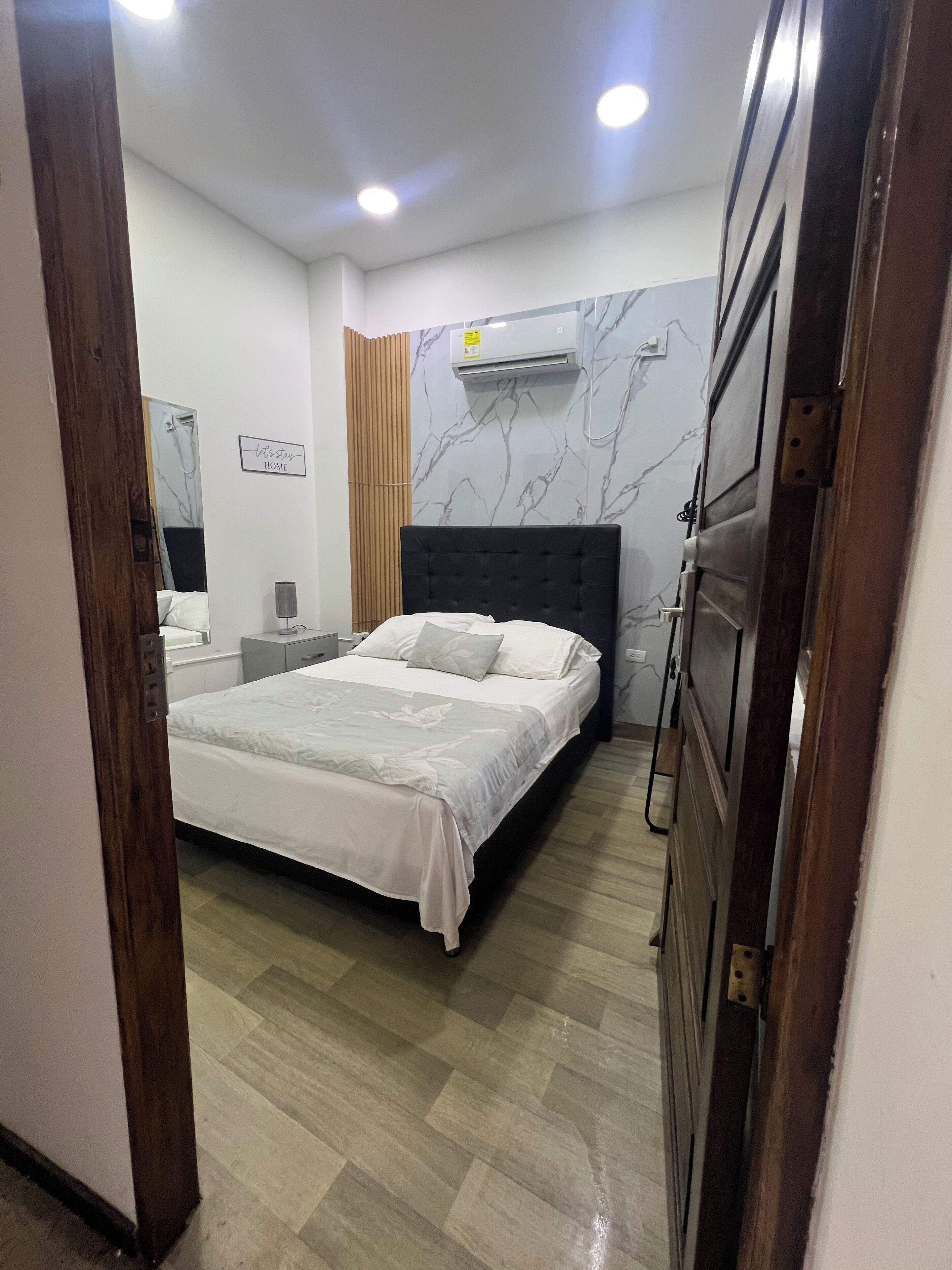 Een slaapkamer met een bed, nachtkastjes, een spiegel, een airconditioning en een deur.