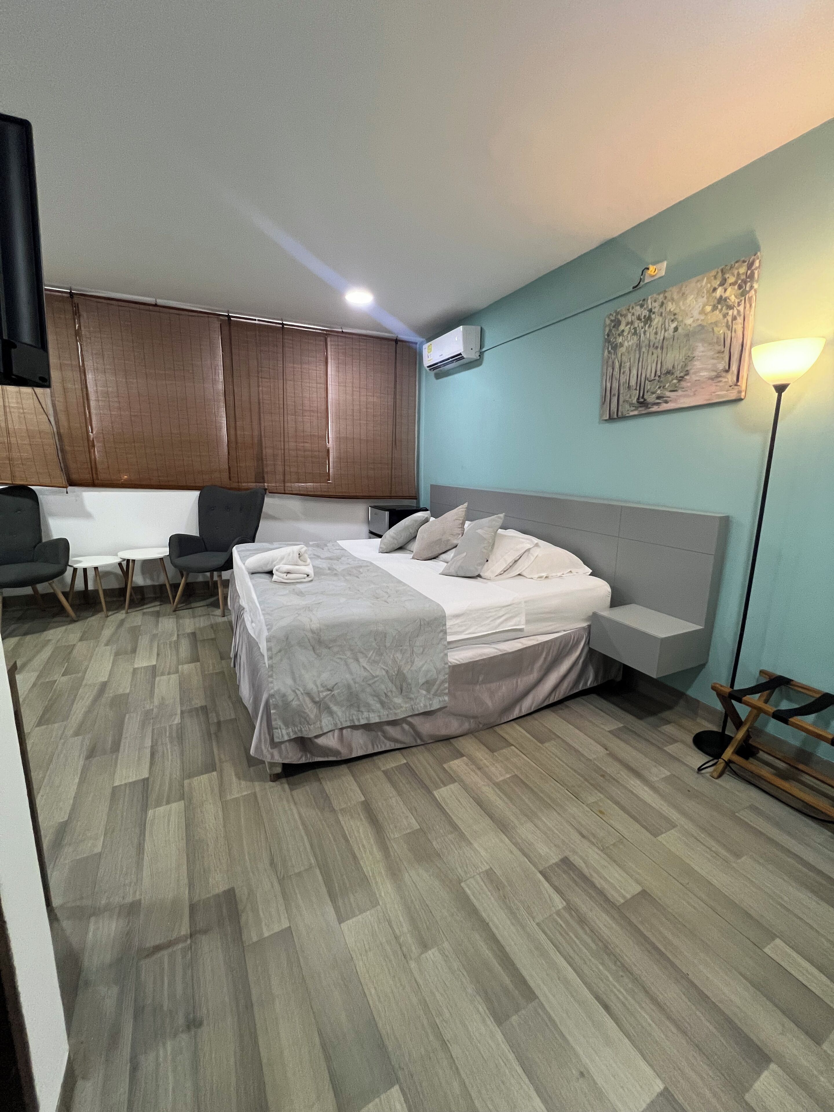 A modern bedroom with a bed, a desk, chairs, and a painting on the wall.