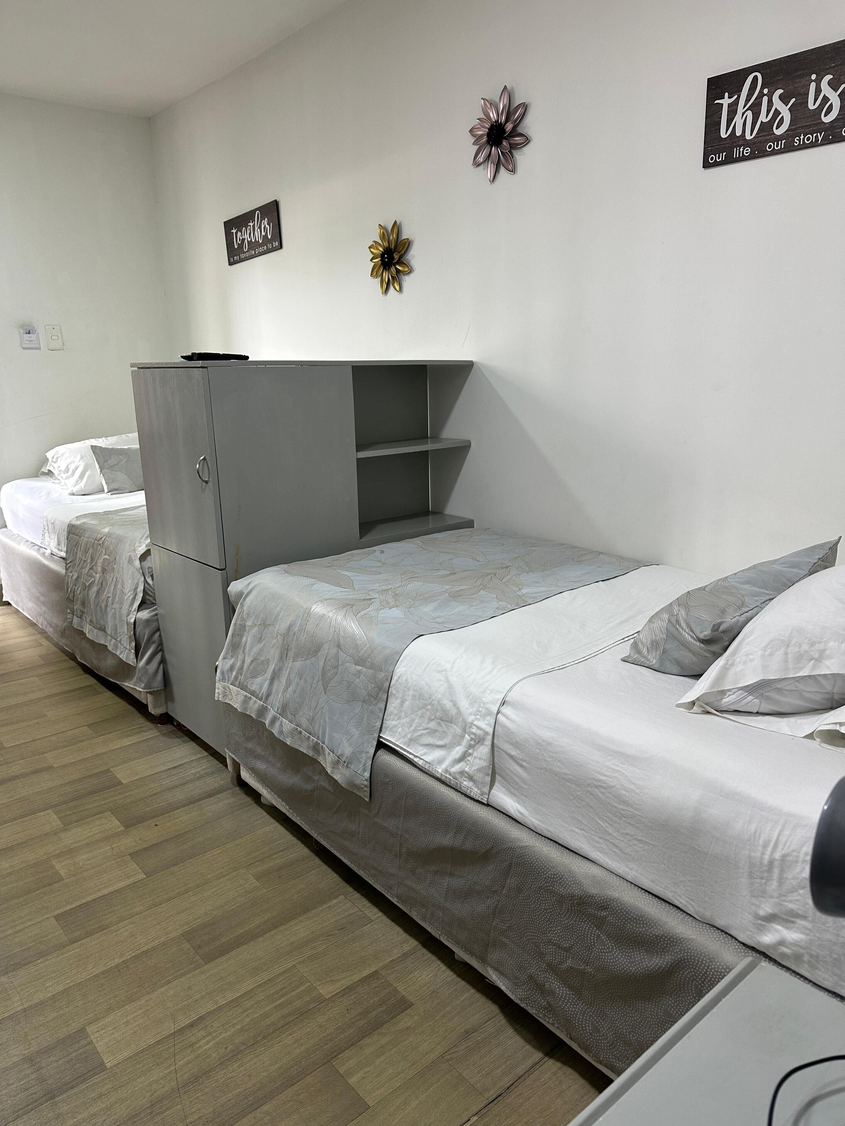 Une chambre de dortoir avec deux lits simples, une armoire grise et une petite étagère.