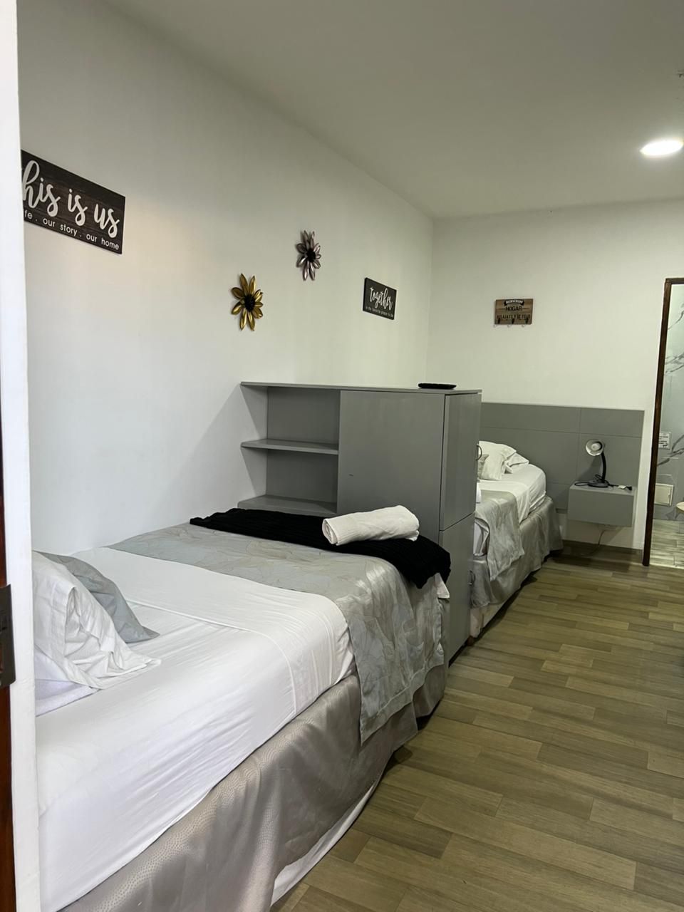 Een hotelkamer met twee bedden, een grijze garderobe, een nachtkastje met een lamp en decoratieve wandkunst.