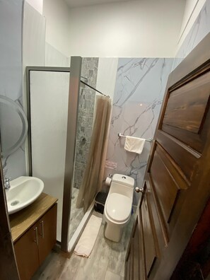 Un baño pequeño con ducha, inodoro, lavabo y armarios de madera.