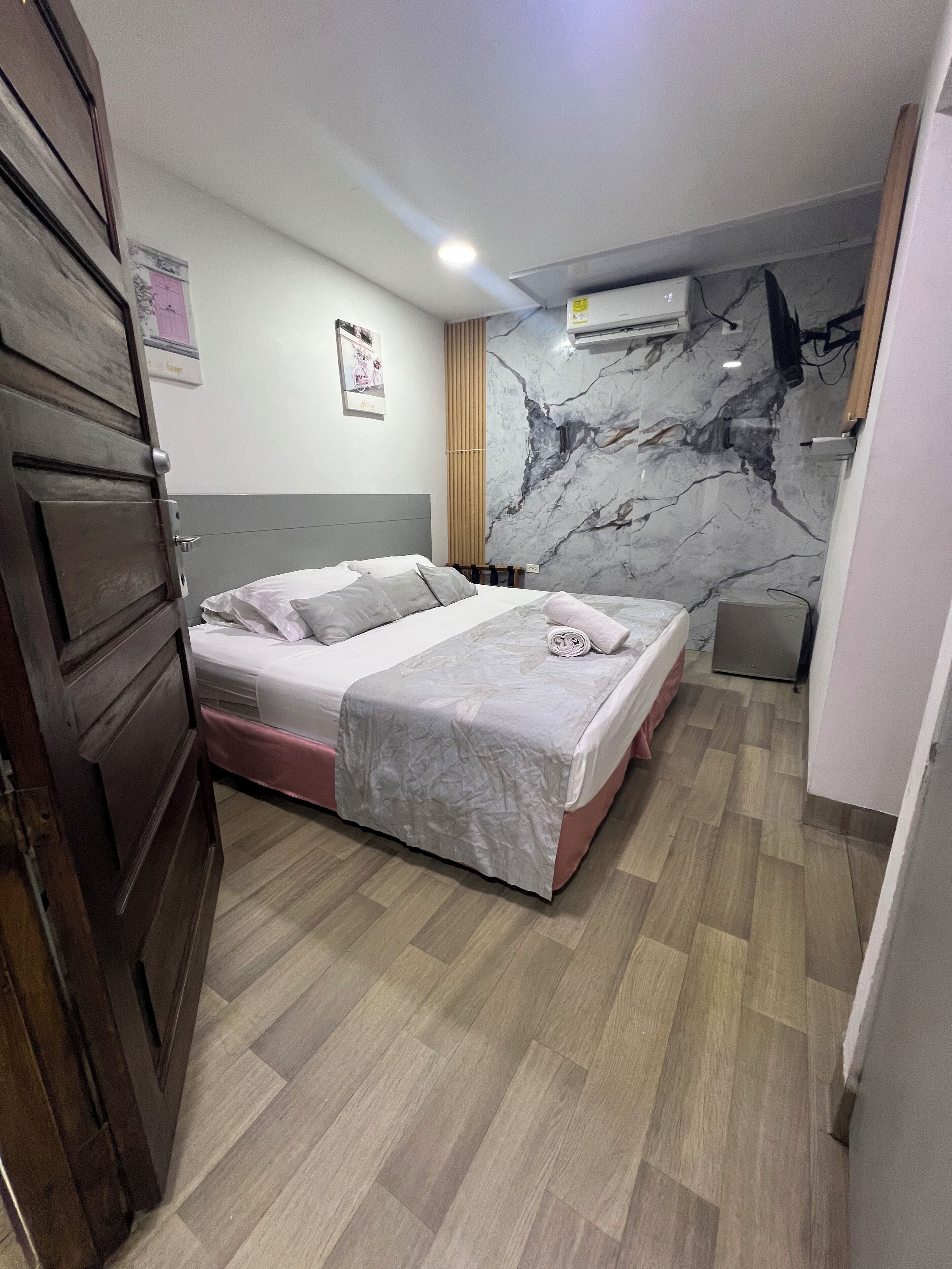 Ein Schlafzimmer mit einem Bett, Holzboden, einer Marmorwand und einer Klimaanlage.