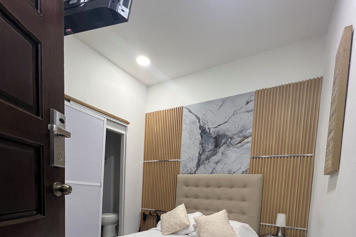 A bedroom with a bed, a nightstand, a wooden panel wall, and a marble wall.