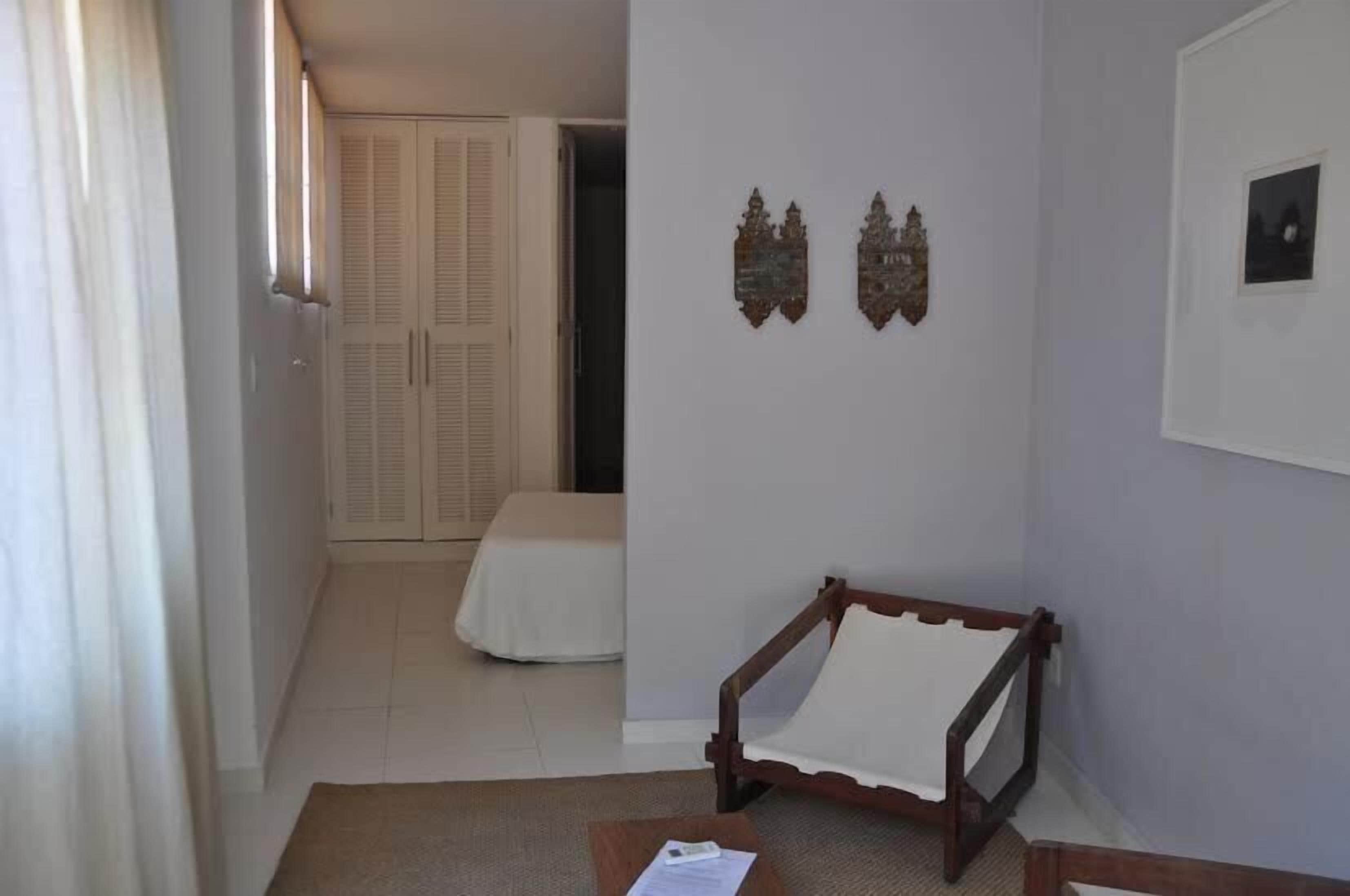 A room with a bed, a wooden chair, a small table, and two wall-mounted decorations.