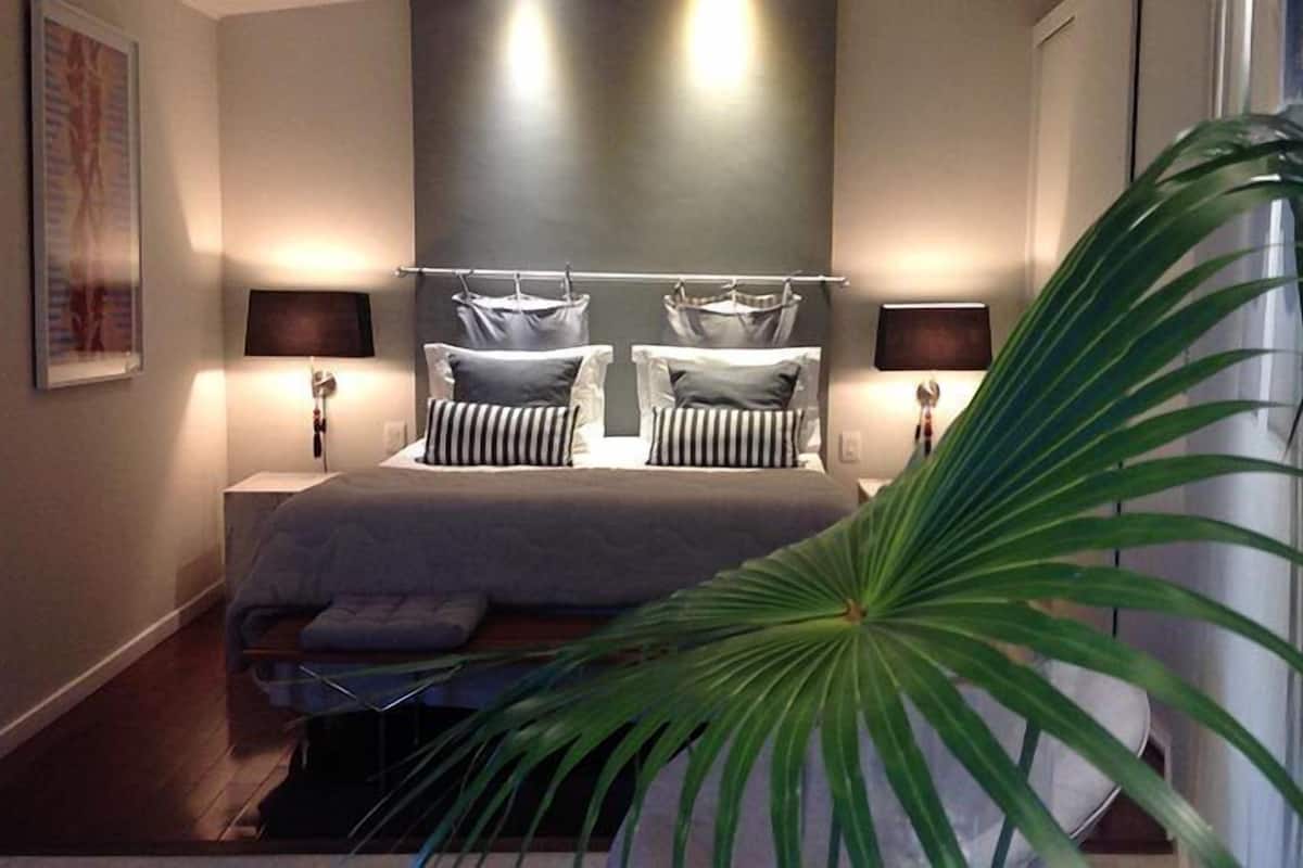 Ein modernes Schlafzimmer mit einem großen Bett, zwei Nachttischen und einer großen Zimmerpflanze.