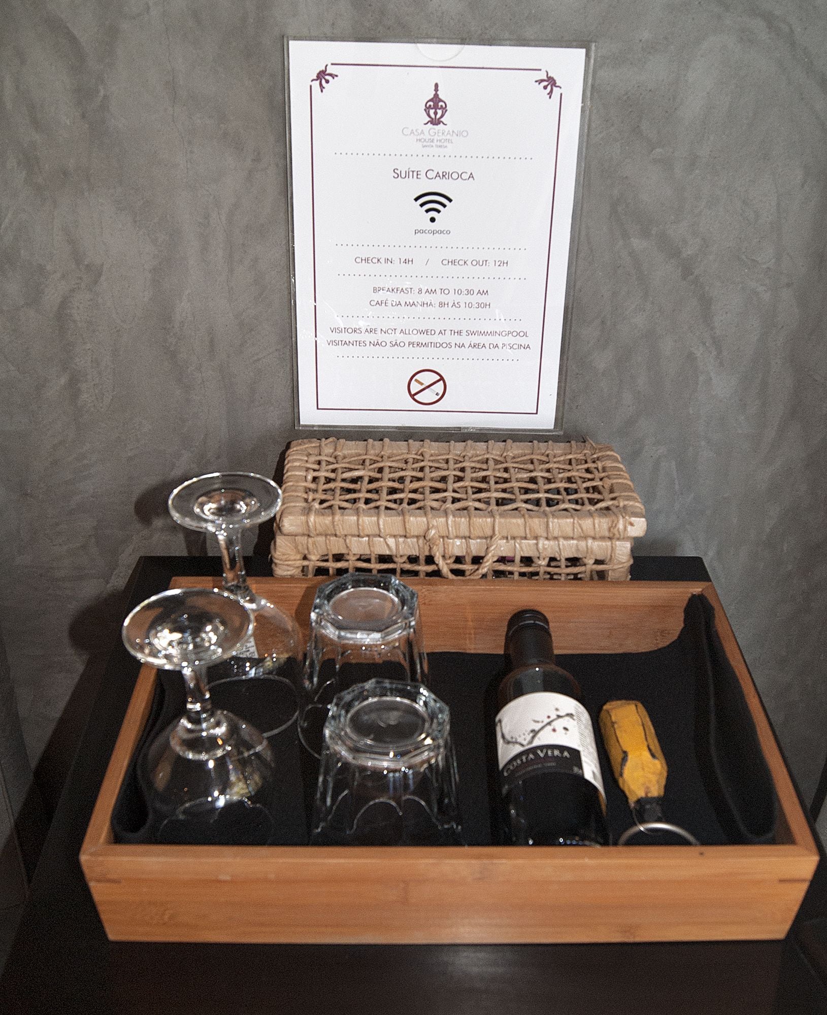 Una bandeja de madera con copas de vino, una botella y un posavasos con el letrero de un hotel y símbolo de Wi-Fi.
