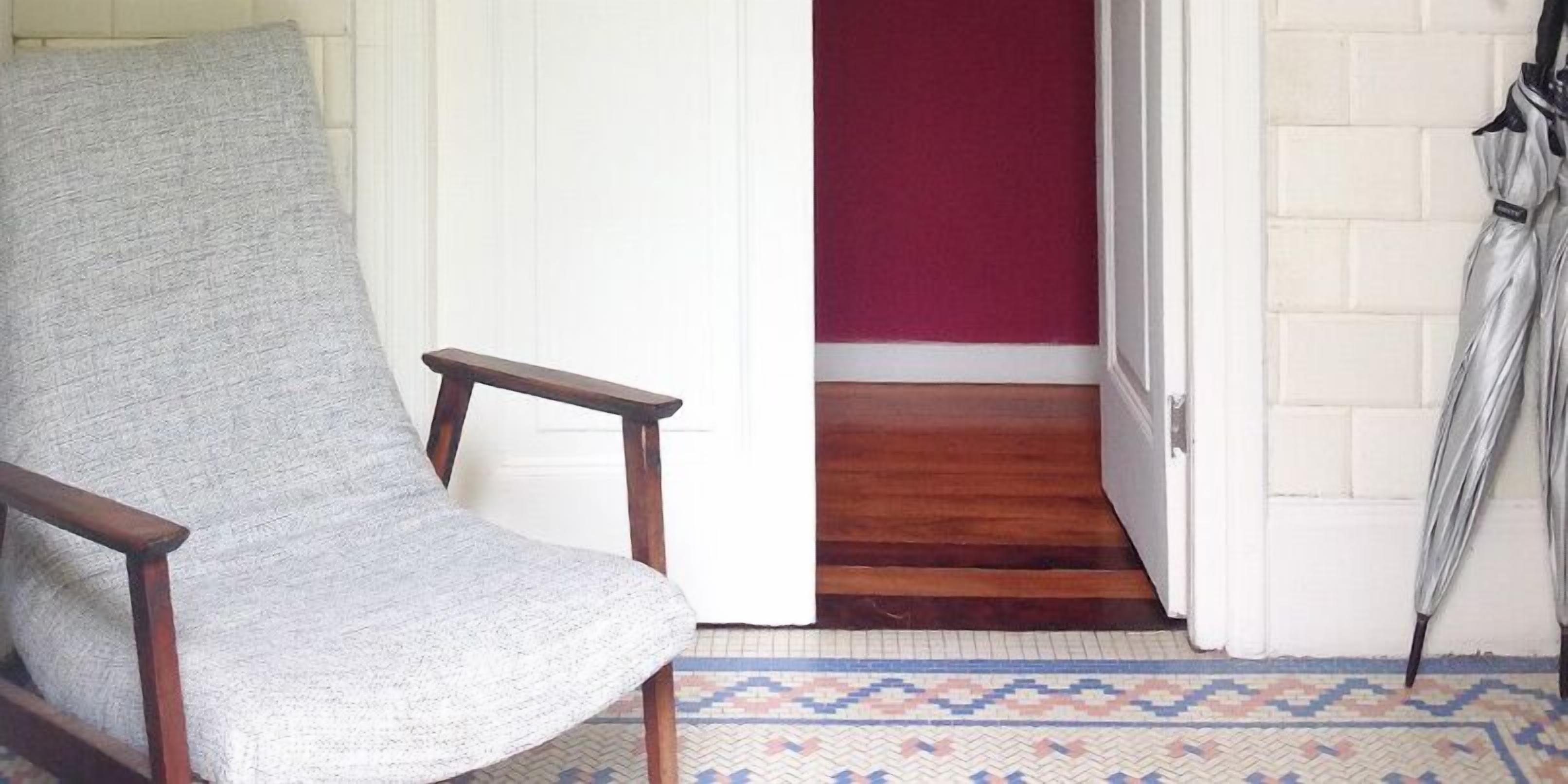 A chair with a grey fabric, a wooden floor, a red wall, and a patterned rug.